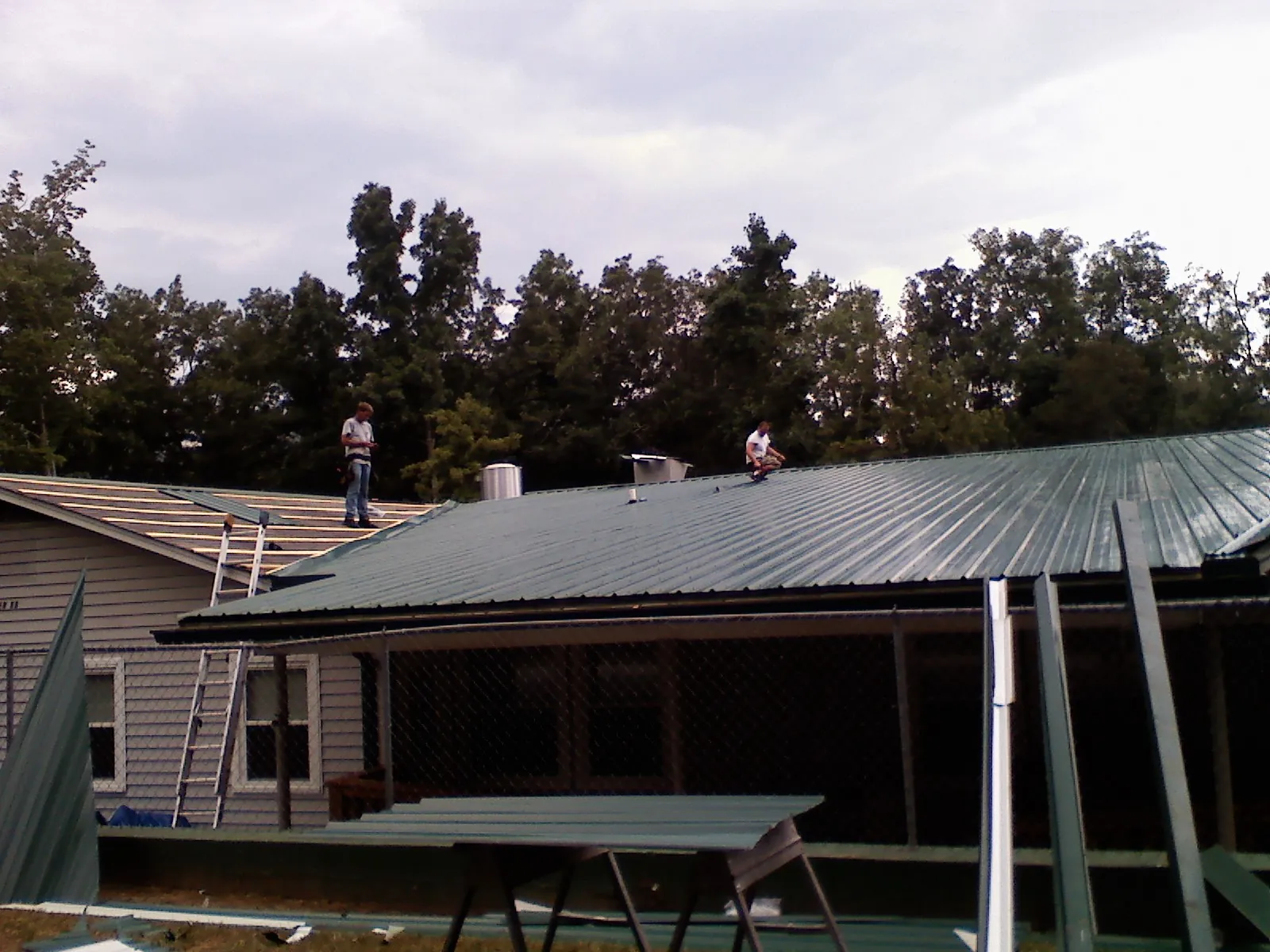 Two roofers installing green metal panels above a covered porch in Prescott Valley