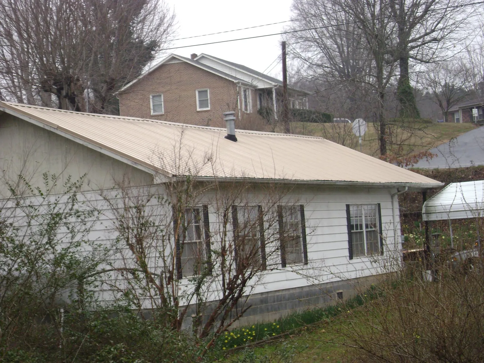 Tan metal roof on a white sided house set into a hillside — Commercial Roofing by Roofing Brothers in Prescott Valley